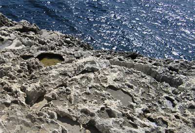 Rainwater is a very weak acid.  It can dissolve limestone and other carbonate rocks leaving behind pits and holes.  Wied-iz-zurrieq, Malta. © Richard Burt